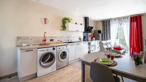 A modern kitchen with a built-in washing machine, a dining area with a table set for two, and a view of the outdoors through large windows.