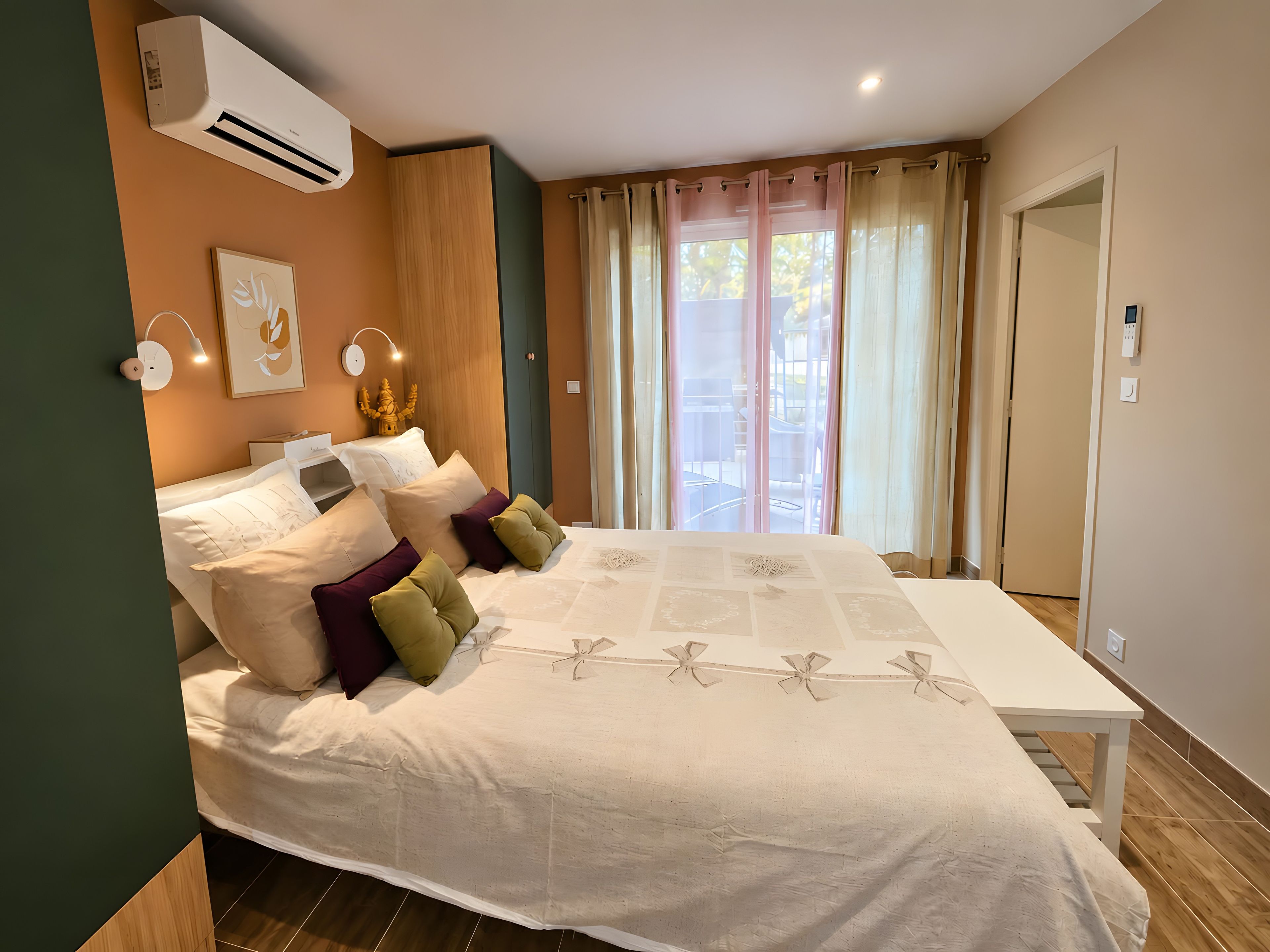 Une chambre à coucher comprenant un lit, des tables de chevet, un appareil de climatisation, une fenêtre avec des rideaux et une vue sur l’extérieur.