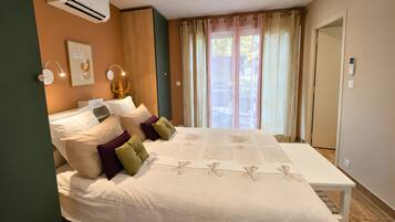 Une chambre à coucher comprenant un lit, des tables de chevet, un appareil de climatisation, une fenêtre avec des rideaux et une vue sur l’extérieur.