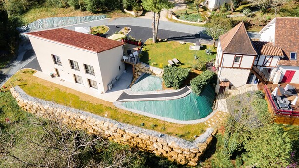 Ein Luftbild eines Wohngebiets mit einem weißen Gebäude, einem roten Dach, einem Swimmingpool und umliegender Bepflanzung.