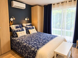 Een slaapkamer met een groot bed, nachtlampjes, een airconditioner en uitzicht op groen buiten.