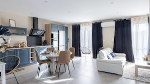 Eine moderne Küche mit Einbauofen und Mikrowelle, ein Essbereich mit rundem Tisch und Stühlen sowie eine Wohnbereich mit Sofa und Couchtisch.