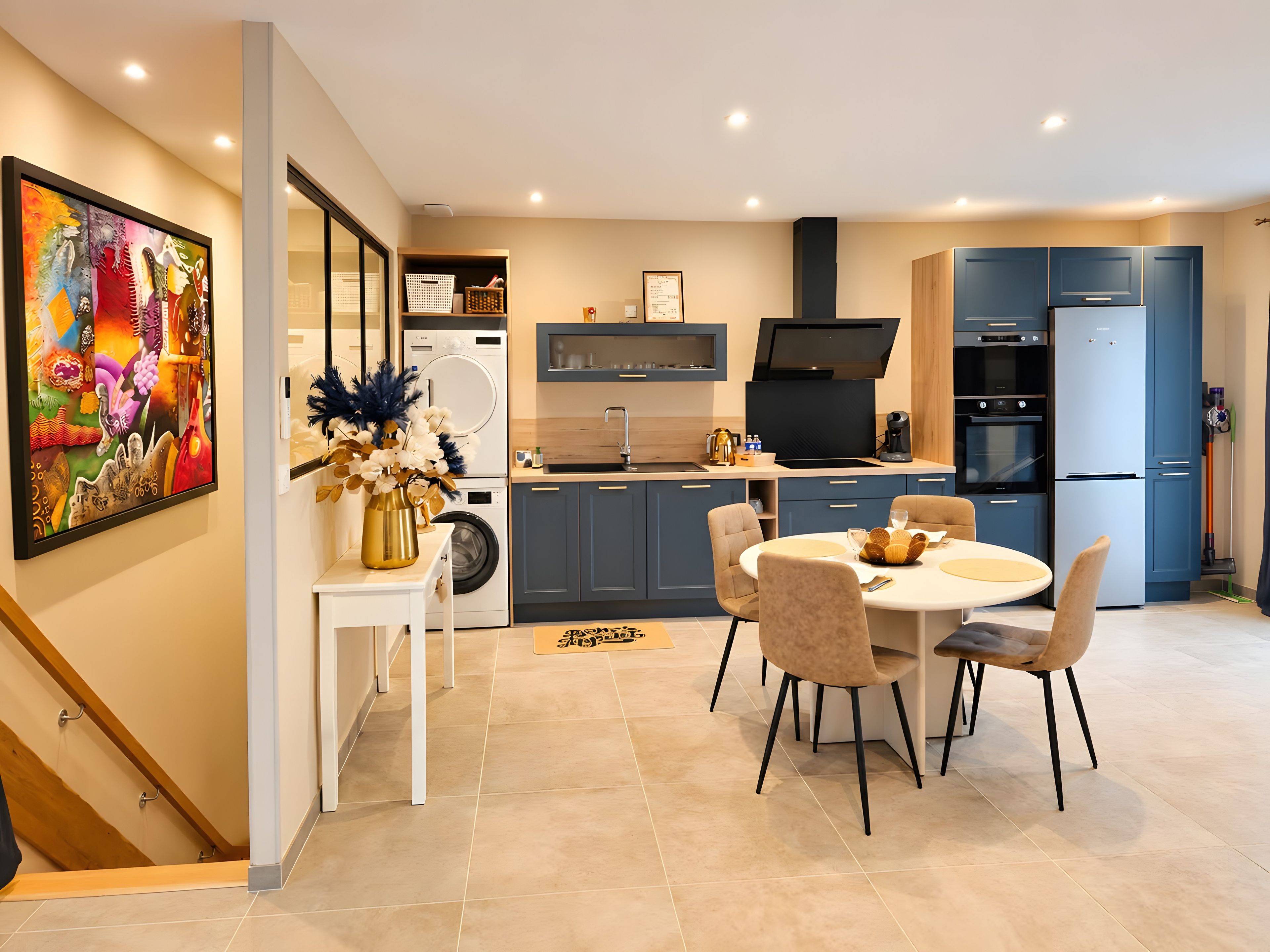 A modern kitchen with a dining area, a washing machine, and a large painting on the wall.