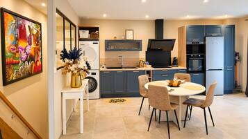 A modern kitchen with a dining area, a washing machine, and a large painting on the wall.