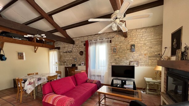 A living room with a red sofa, a black leather chair, a television, a fireplace, and a stone wall.