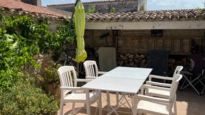 A patio with a table and chairs, a yellow umbrella, and a stone wall with a chimney.