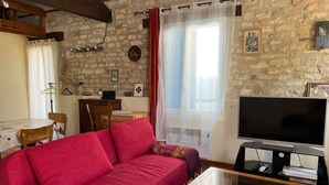 A cozy living room with a red sofa, a television, and stone walls.