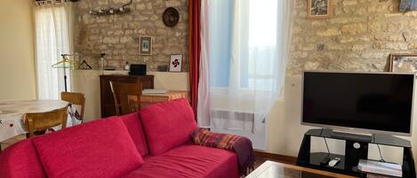 A cozy living room with a red sofa, a television, and stone walls.
