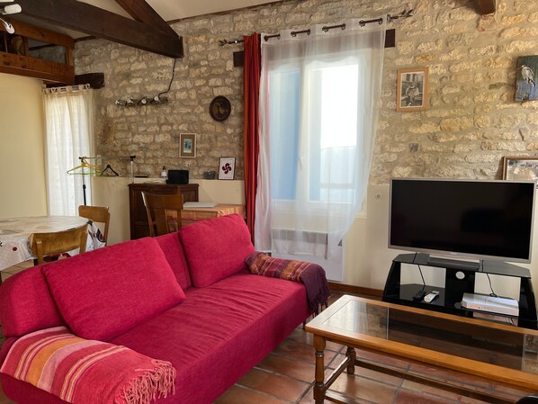 A cozy living room with a red sofa, a television, and a stone wall.