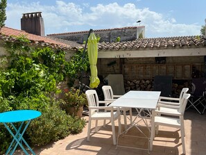 Un patio con una mesa y sillas, un paraguas amarillo y un muro de piedra.
