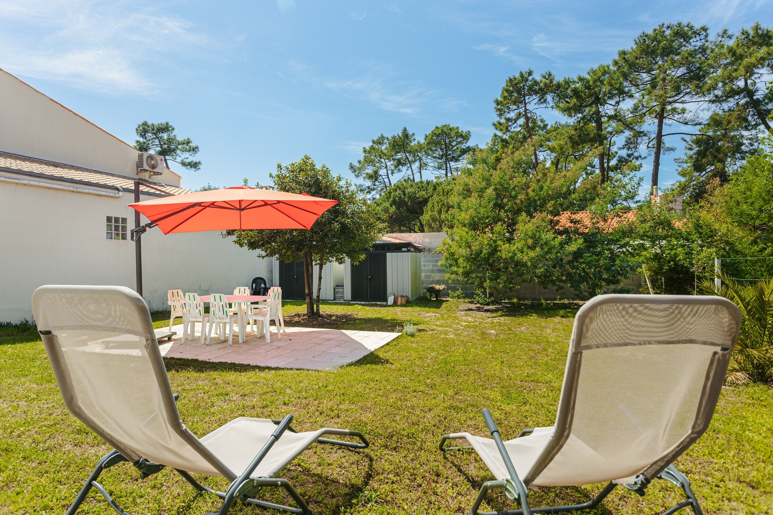 A backyard with two lawn chairs, a red umbrella, and a patio table.