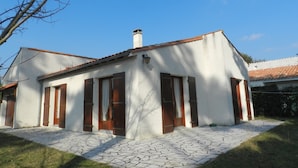 A single-story building with a tiled roof, a chimney, and a paved entrance area. - Holiday Home 'Maison À 8min De Plage Giraudière' with Private Terrace and Private Garden (Le Grand-Village-Plage)