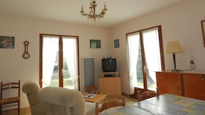 A room with a dining table, chairs, a television, a clock, and a chandelier. - Holiday Home 'Maison À 8min De Plage Giraudière' with Private Terrace and Private Garden (Le Grand-Village-Plage)