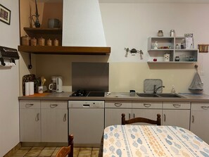 Une cuisine compacte équipée d’un lave-vaisselle, d’une cuisinière et d’un évier. On y trouve une chaise en bois et un lit recouvert d’une courtepointe à motifs.