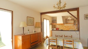 A dining area with a table set for four, a wooden cabinet, and a kitchen visible through an open doorway. - Holiday Home 'Maison À 8min De Plage Giraudière' with Private Terrace and Private Garden (Le Grand-Village-Plage)