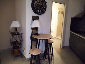 Une cuisine avec une table ronde, deux tabourets, une horloge et un téléviseur.