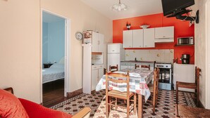 A compact kitchen with white cabinets, a microwave, and a stove. There is a dining table with chairs, a red sofa, and a patterned floor. - Peaceful Holiday Home with Private Courtyard – Close to Beaches and Shops in Saint-Trojan (Saint-Trojan-les-Bains)