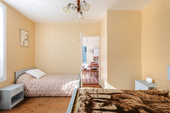 Un dormitorio con dos camas, piso de madera, ventilador de techo y puerta que da a un baño.