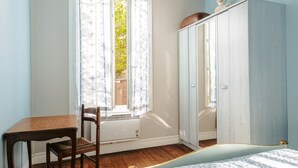A room with a bed, a wooden table, a chair, a wardrobe, and a window with curtains. - Peaceful Holiday Home with Private Courtyard – Close to Beaches and Shops in Saint-Trojan (Saint-Trojan-les-Bains)