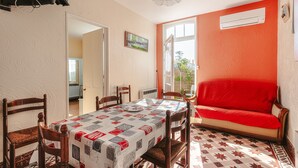 A dining area with a table set for four, wooden chairs, a red sofa, and a patterned tablecloth. - Peaceful Holiday Home with Private Courtyard – Close to Beaches and Shops in Saint-Trojan (Saint-Trojan-les-Bains)