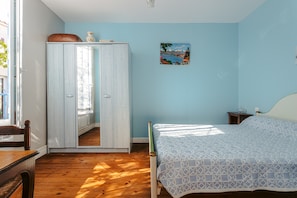 A bedroom with a bed, a wardrobe, a small table, and a painting on the wall.