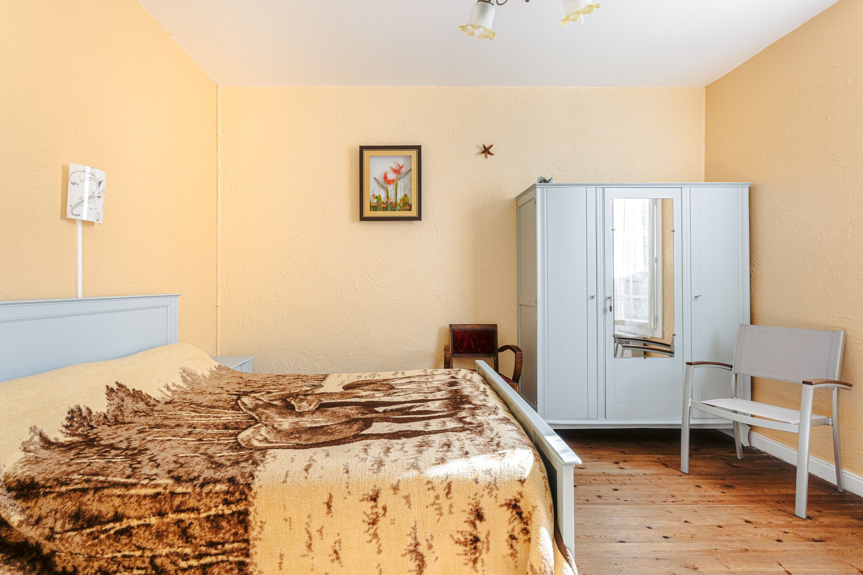 Un dormitorio con cama, armario, silla y un cuadro en la pared.
