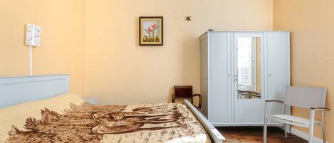 Un dormitorio con cama, armario, silla y un cuadro en la pared.
