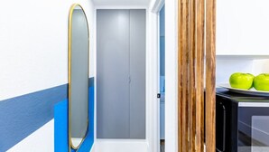 Un pasillo estrecho con pared azul y blanca, una puerta gris y un panel de madera a la derecha.