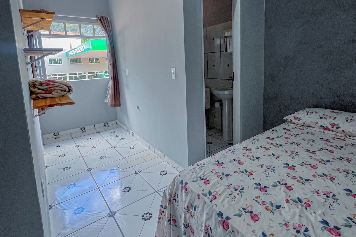 A bedroom with a bed, a window, and a bathroom visible through an open door.