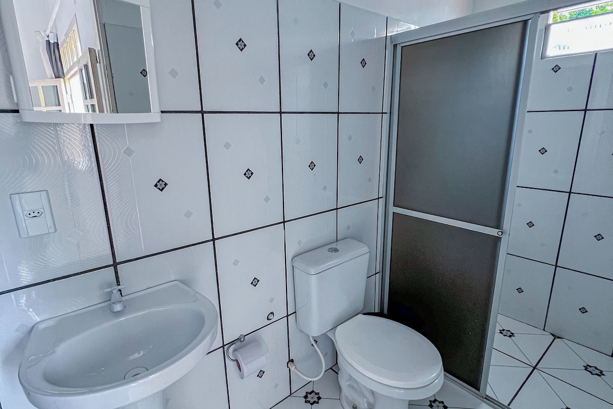A bathroom with a white sink, toilet, and shower. The walls are tiled with a geometric pattern.