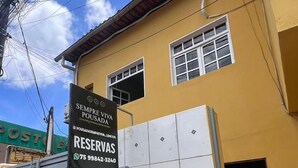 A yellow building with a sign for 'RESERVAS' and a contact number. - Pousada Sempre Viva Lençóis (Lençóis)