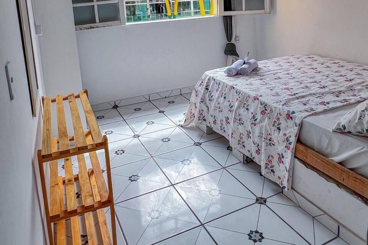 A bedroom with a bed, a window, a wooden bench, and a tiled floor.