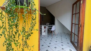 A yellow exterior wall with a hanging plant, a tiled floor, a white desk with a chair, and a door leading to an interior space. - Pousada Sempre Viva Lençóis (Lençóis)