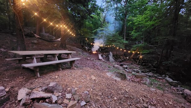 A rustic picnic area with a wooden table and benches, surrounded by trees and a rocky path. - Beautiful mountainside hobby farm with gorgeous view! (Jasper)