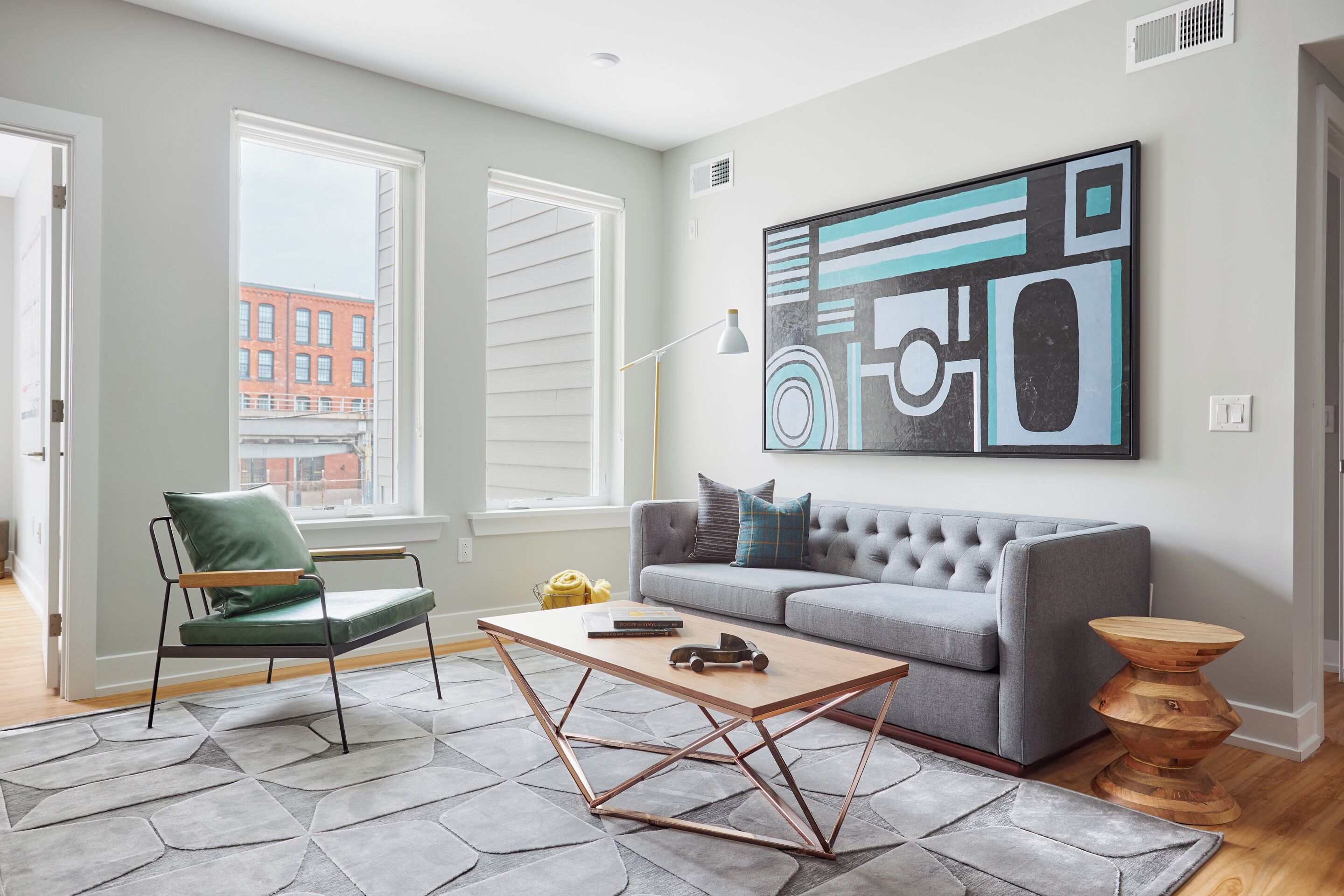 Ein modernes Wohnzimmer mit grauem Sofa, einem grünen Sessel, einem Holztisch und einem großen, abstrakten Gemälde an der Wand.
