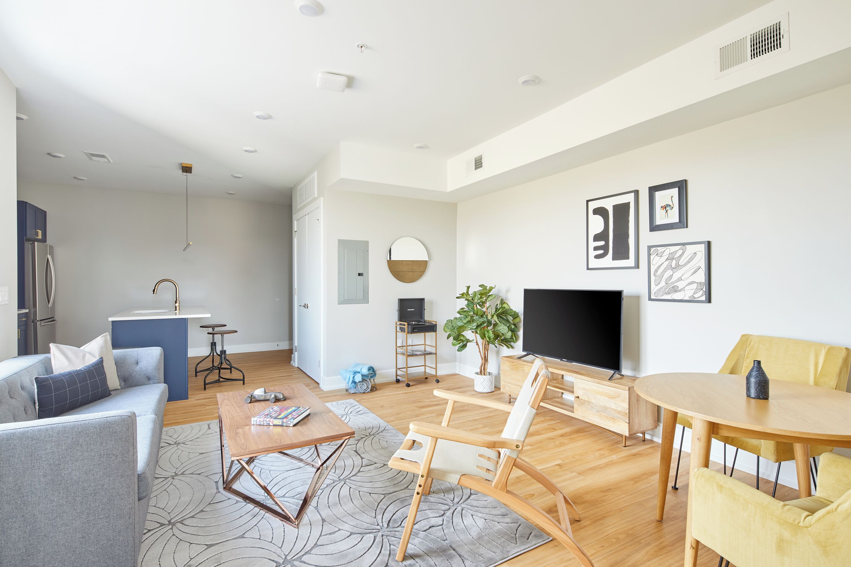 Un salon moderne avec un canapé, une table basse et un téléviseur. Il y a également un coin cuisine équipé d’un réfrigérateur et d’un évier.