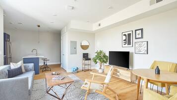 Un salon moderne avec un canapé, une table basse et un téléviseur. Il y a également un coin cuisine équipé d’un réfrigérateur et d’un évier.