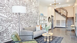 A modern living room with a patterned wall, a grey sofa, a green armchair, and a coffee table. - StayCozy at The Frankford (Philadelphia)