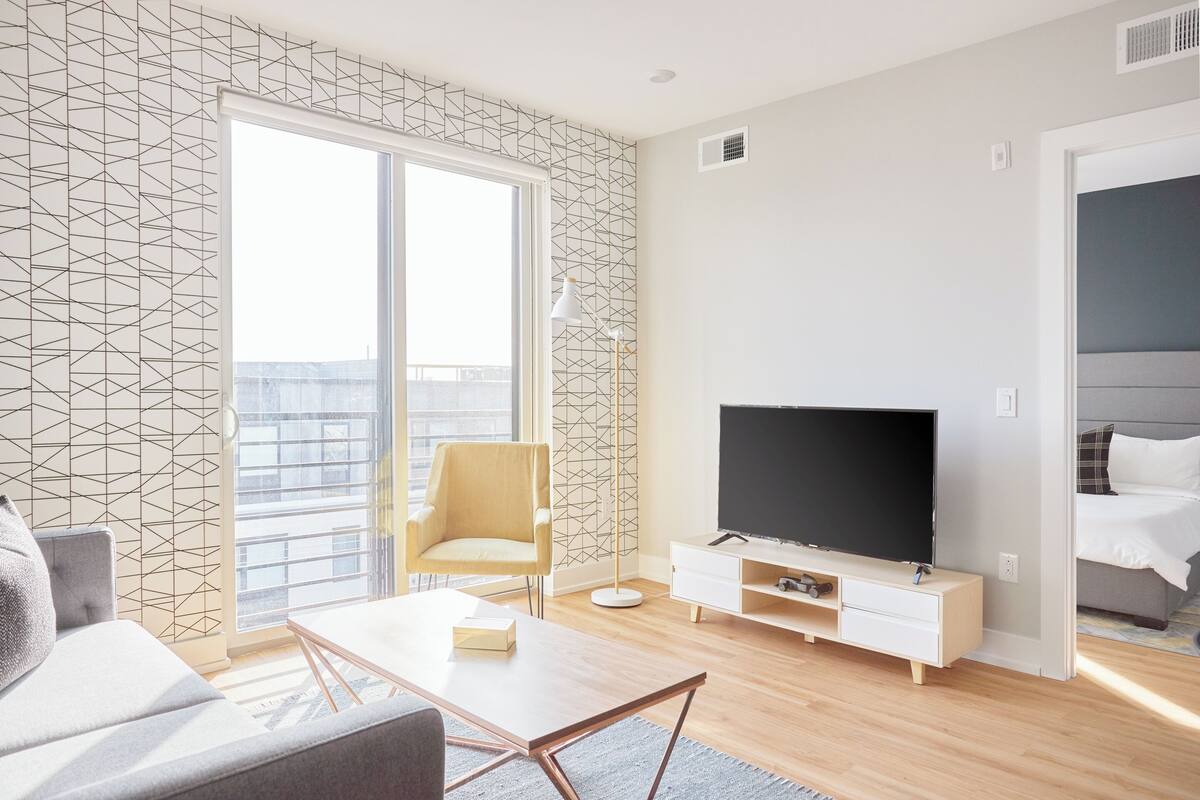 A modern living room with a large window, a flat-screen TV, a sofa, a coffee table, and a chair.