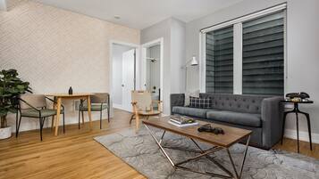 A modern living room with a grey sofa, a wooden coffee table, and a dining area with a table and chairs.