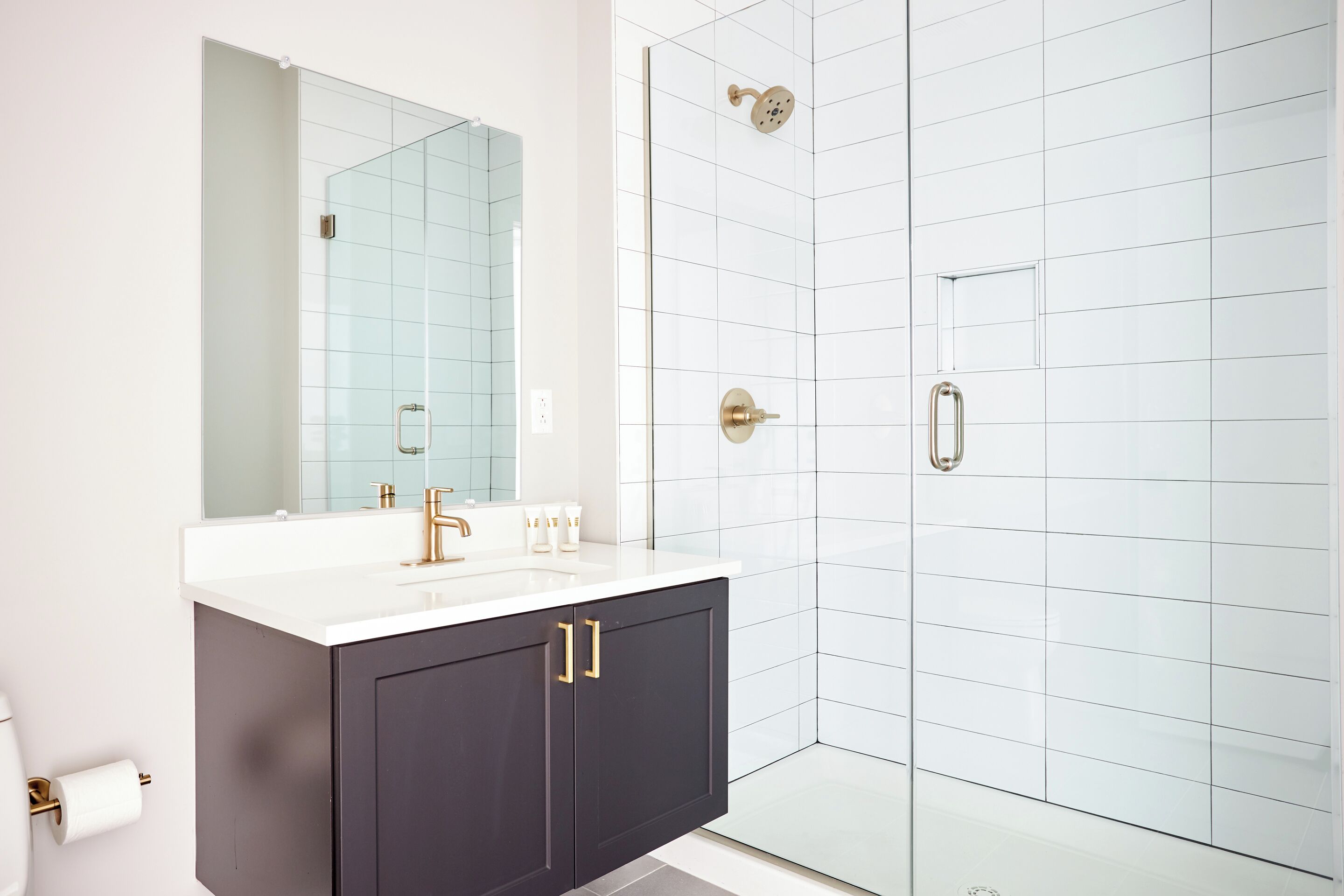 A modern bathroom with a white sink, dark cabinets, and a glass shower enclosure.