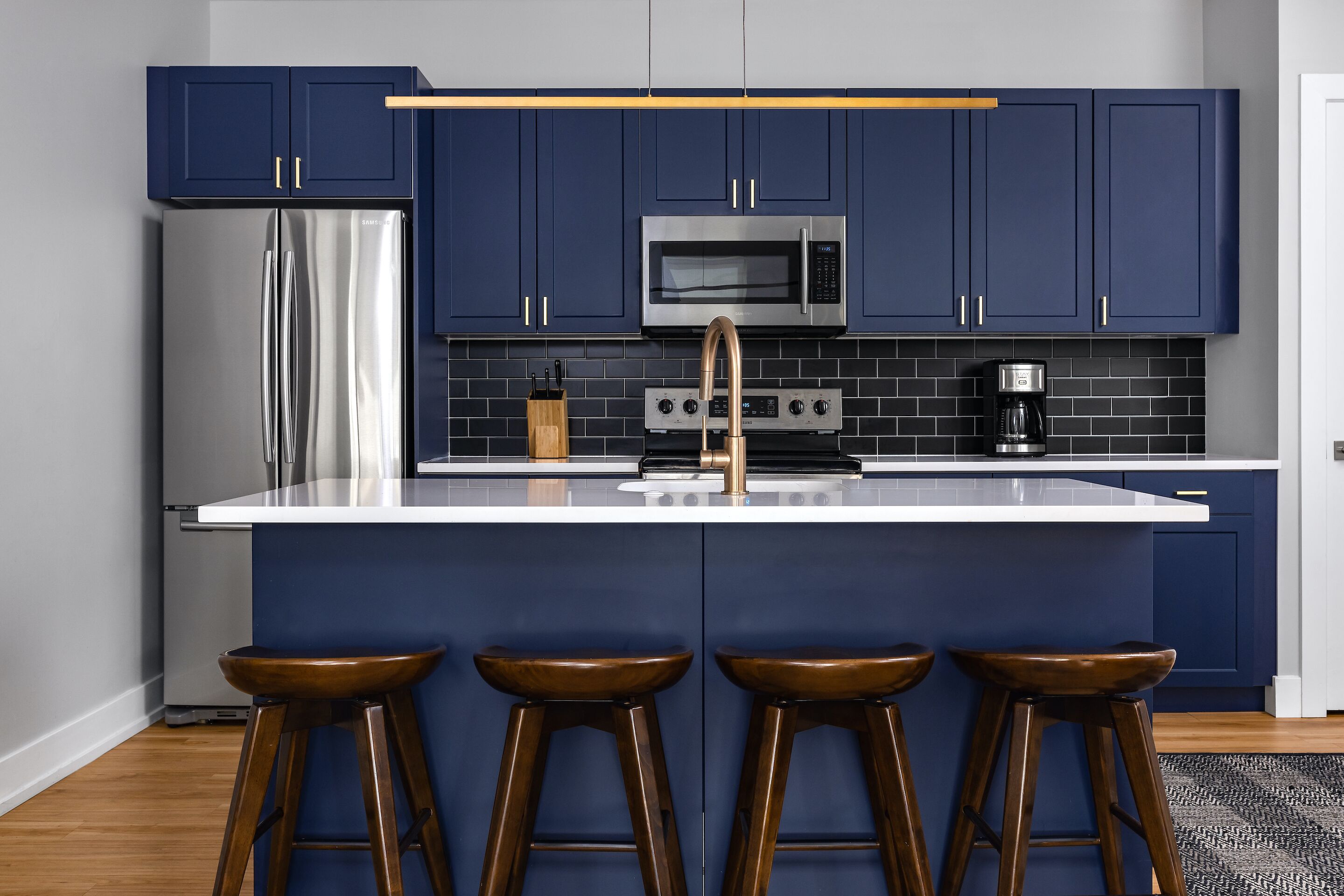 Cocina moderna con armarios azul oscuro, electrodomésticos de acero inoxidable y encimera blanca.