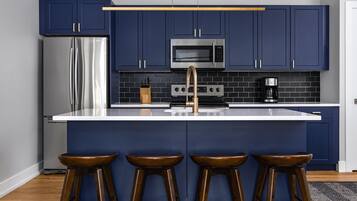 Cocina moderna con armarios azul oscuro, electrodomésticos de acero inoxidable y encimera blanca.