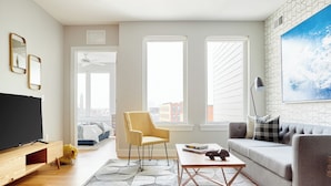 A modern living room with a flat-screen TV, a sofa, a yellow armchair, and a coffee table. - StayCozy at The Frankford (Philadelphia)
