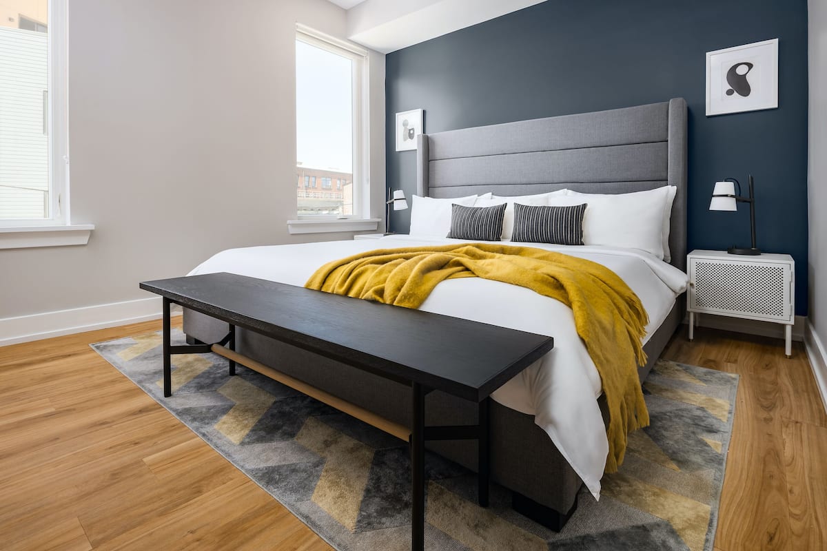 A modern bedroom with a large bed, a bench, a nightstand, and a window.