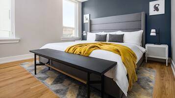 A modern bedroom with a large bed, a bench, a nightstand, and a window.