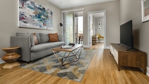 A modern living room with a grey sofa, a wooden coffee table, and a flat-screen TV on a wooden stand. - StayCozy at The Frankford (Philadelphia)