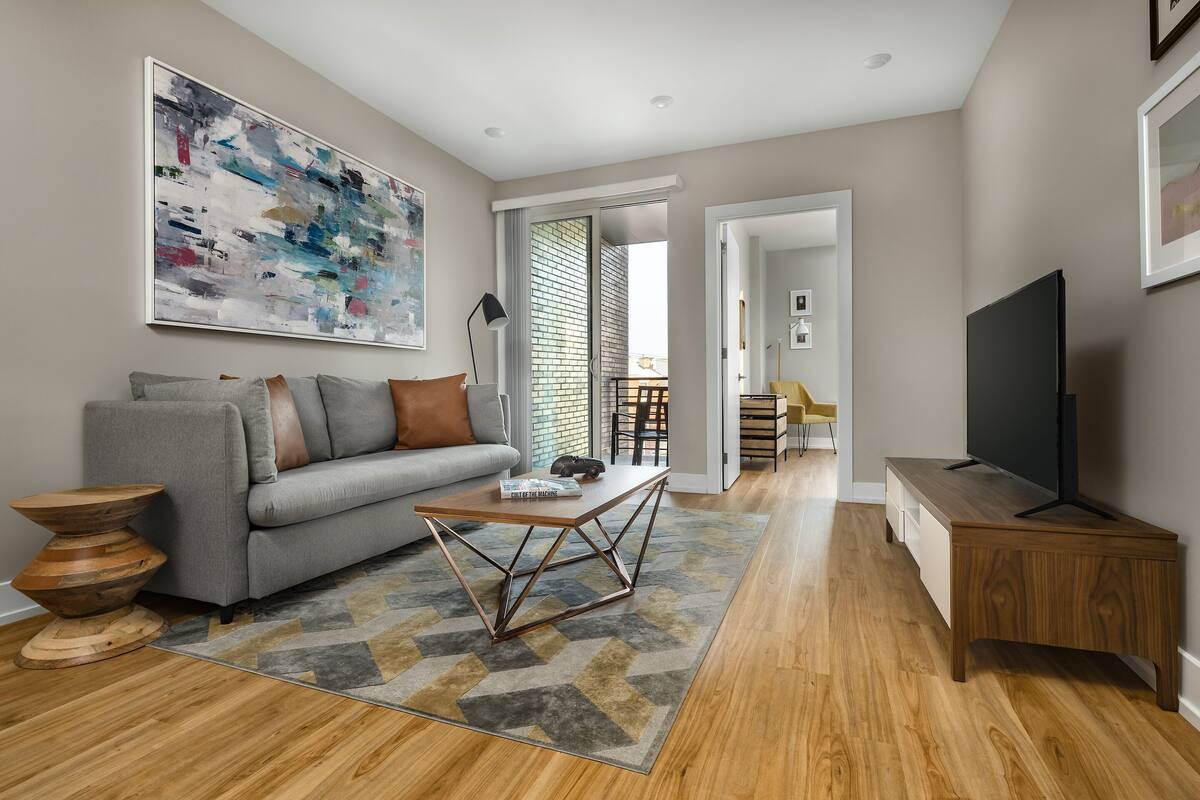 A modern living room with a grey sofa, a wooden coffee table, and a flat-screen TV on a wooden stand.