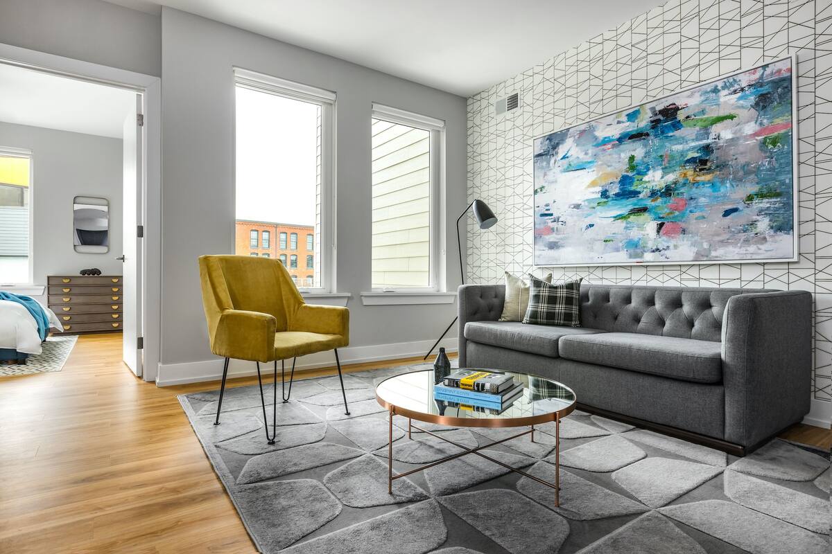 A modern living room with a grey sofa, yellow armchair, and a glass coffee table.