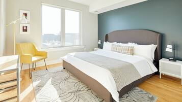 A modern bedroom with a large bed, a view of the city, a yellow chair, and a white desk.
